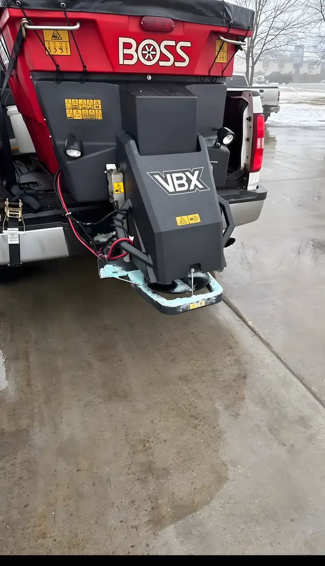 Red BOSS salt spreader mounted on the back of a plow truck