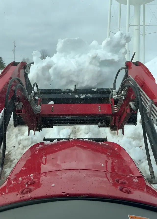 A red loader lifting a bucket full of snow