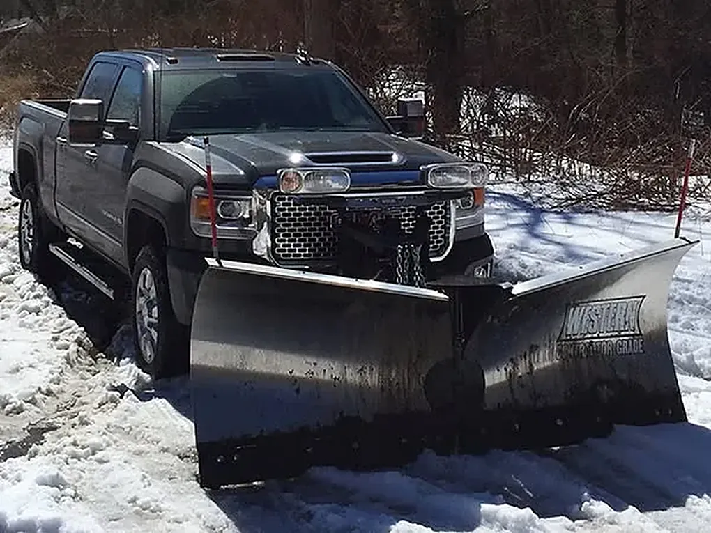 Dark GMC pickup with a Western straight-blade plow on a snowy road